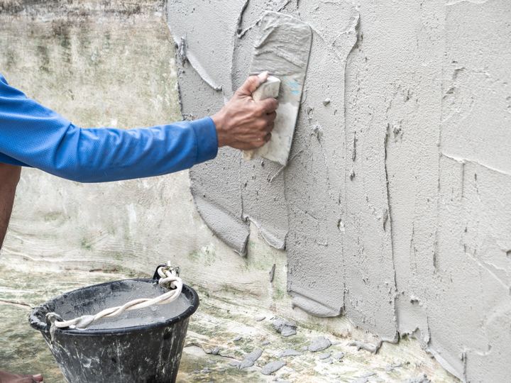 A mason smoothing a fresh parge coat over a concrete foundation wall with a trowel.